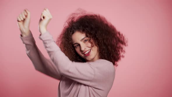 Beautiful Woman with Curly Hair Dancing with Head on Pink Studio Background.