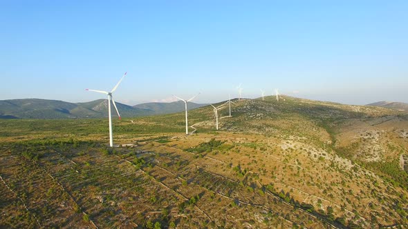 Flying above a group of white wind turbines with red tip blades on a sunny day