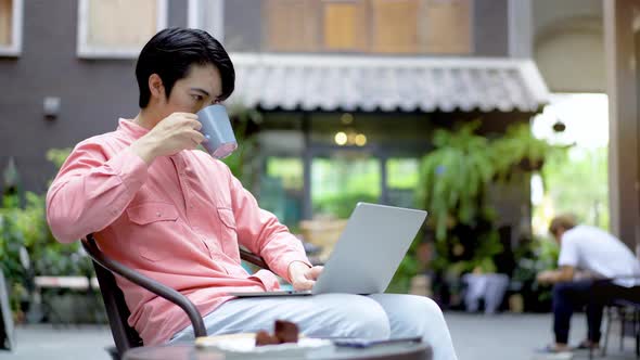 Young asian man smiling confident working on laptop with cup of coffee at outdoor cafe