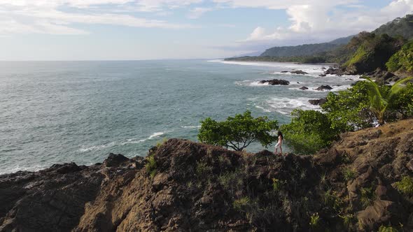 Lady walking on cliff edge with view of ocean in Costa Rica. Aerial tracking shot