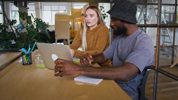 Young Office Manager Talking to African American Client Showing Him Marketing Strategy on Laptop