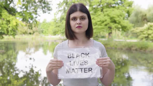 A Young Caucasian Woman Shows a Black Lives Matter Sign to the Camera in a Park