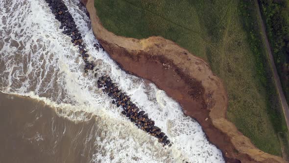 Aerial drone footage top down on high tide as the sea crashes into sea defences. The camera then and