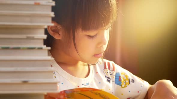 A little cute girl reading a book sits on table at home.