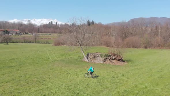 Aerial: man having fun by riding mountain bike in the grass on sunny day, scenic alpine landscape