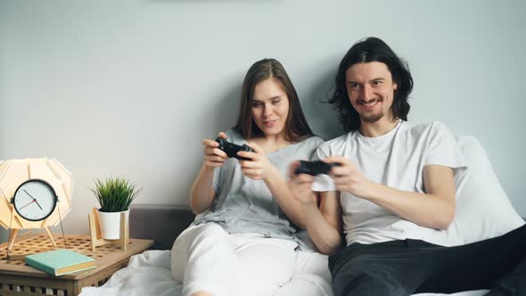 Cute Young Couple Boyfriend and Girlfriend Are Playing Videogame on Bed at Home