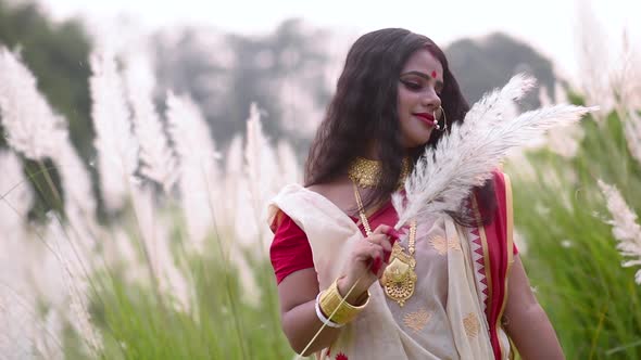 A cute and carefree newly wed Indian woman is happy and plays with white flowered grass in a field o