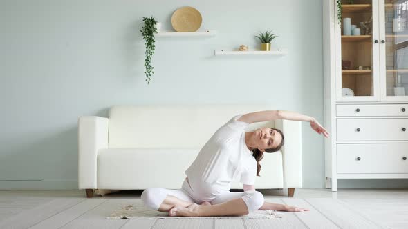 Brunette Pregnant Woman Does Side Bends on Floor at Home