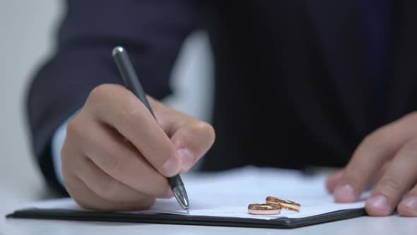 Lawyer Writing Marriage Contract, Two Wedding Rings Lying on Document, Divorce