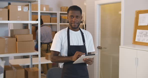 Portrait of Young Mixedrace Man Using Digital Tablet in Warehouse Doing Inventory Smiling at Camera