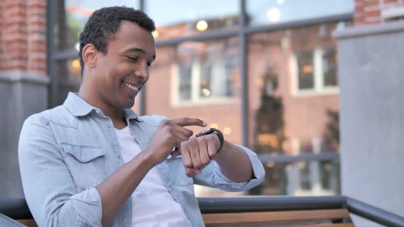 African Man Using Smartwatch Sitting Outdoor