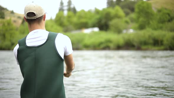 Shot of a Caucasian male fisherman casting his hook while Fly Fishing. He is standing in the middle