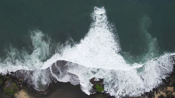 Top down aerial view of giant ocean waves crashing and foaming in coral beach