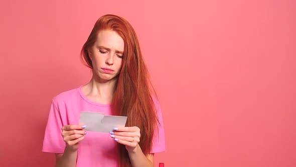 Redhaired Ginger Woman in Pink Studio Background Tearing Photo Card of Smiling International Couple