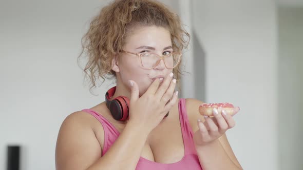 Plus-size Coquette Woman Tasting Delicious Donut and Smiling at Camera. Close-up Portrait of