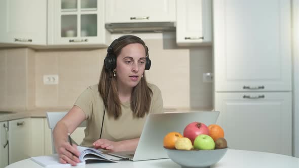 Young woman in headphones working on a laptop in the kitchen