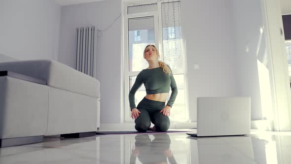 young blonde woman in sportswear practicing yoga online using video tutorials.