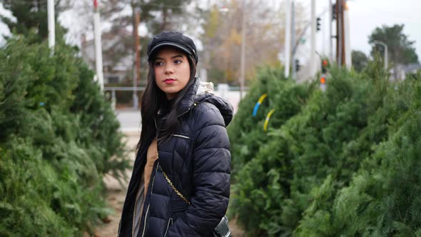 A hispanic woman shopping for a seasonal holiday Christmas tree decoration on a lot with many specie