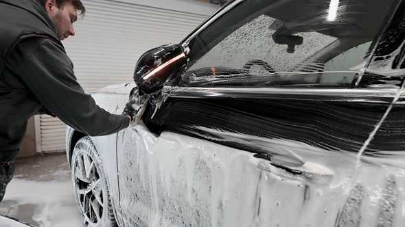 Male Worker in Black Glove with Foam Sponge Washing Car at Car Service Car Wash