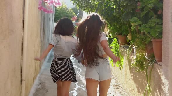 Two Girls Running Across Sunny Street in Greece
