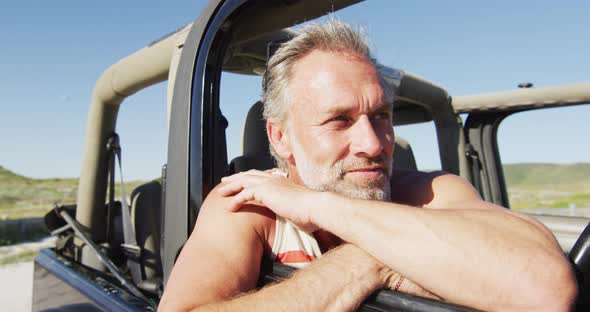 Happy caucasian man sitting in car enjoying the view on sunny day at the beach