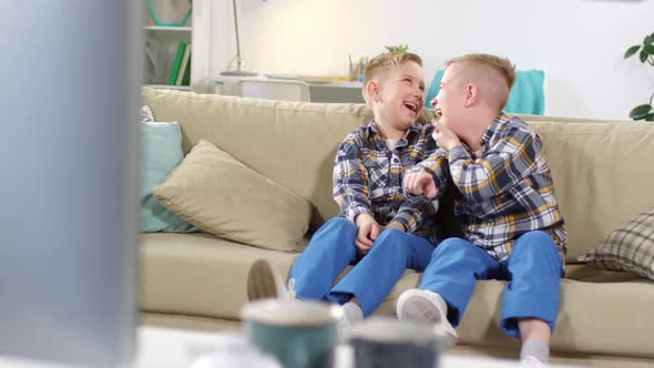 Caucasian Identical Twins Watching TV and Rolling with Laughter