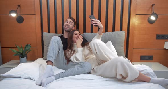 Young Couple Takes a Selfie on a Smartphone Man and a Woman Lying on the Bed and Shoot a Video on a