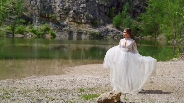 The Bride in a White Wedding Dress Walks Along the Bank of a Mountain River