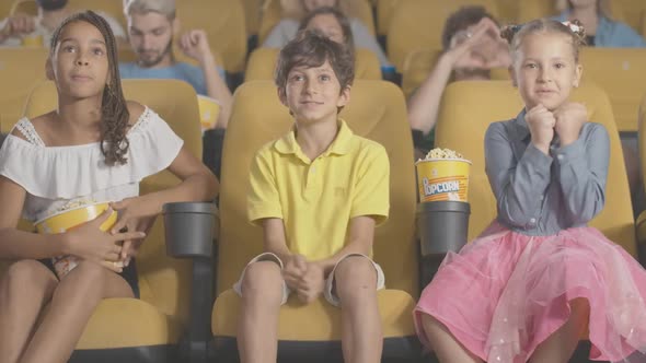 Three Excited Children of Different Ethnicities Watching Film in Cinema with Blurred People at the