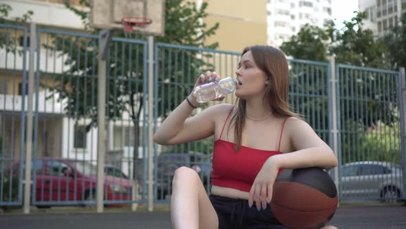 Young Woman Teenager Drinks Water From a Bottle on a Basketball Court Outdoors