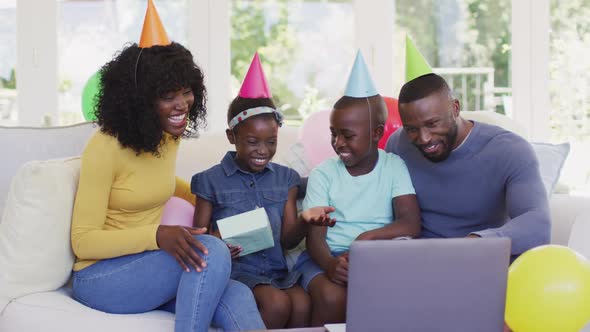 African american family in party hats waving having a videocall on laptop while sitting on the couch