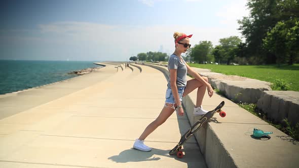 A young woman stretching next to her longboard skateboard.