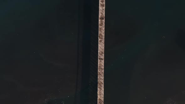 A high drone view of a long boardwalk jetty out to sea with polluted water surrounding it