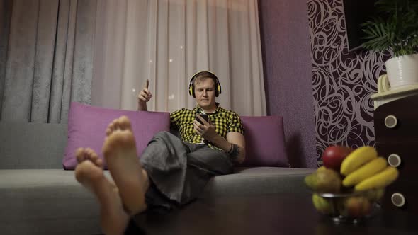 Man Lying on the Sofa Listens Music with Wireless Headphones and Dances