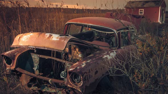 Abandoned vintage car sit dilapidated in a tall grass field, coated in the warm glow from the settin