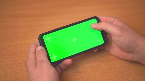 Top view of male hands holding mobile phone with green mock up screen.