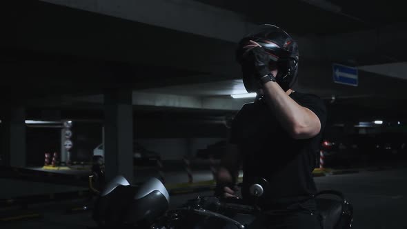 A Man Sitting on a Motorcycle Takes Off His Helmet in Underground Parking Garage Slow Motion