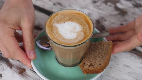 Hands Taking Away a Glass of Vegan Cappuccino with Heart Art on It