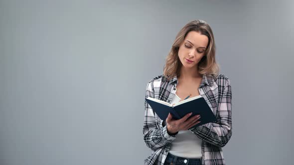 Playful Young Woman Writing Notes in Paper Notebook Use Pen Smiling Having Positive Emotion