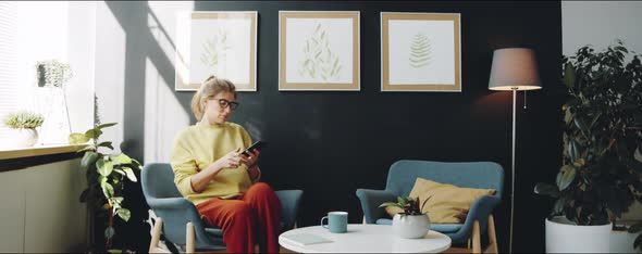 Woman Using Smartphone and Drinking Coffee at Home