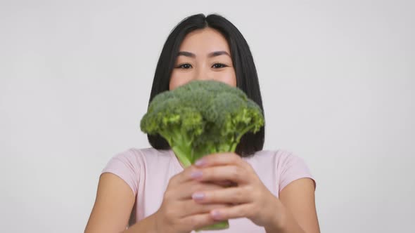 Smiling Japanese Female Offering Broccoli To Camera On White Background