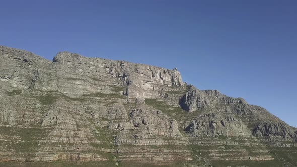 Aerial lower angle scenic drone flight view of Table Mountain in late afternoon sun against blue sky