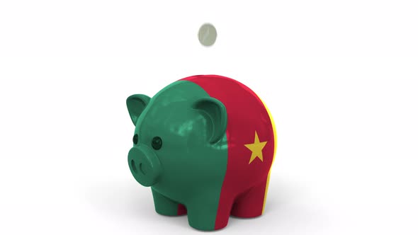 Coins Fall Into Piggy Bank Painted with Flag of Cameroon alt
