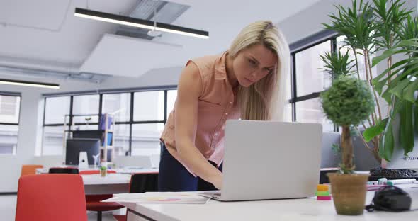 Caucasian businesswoman using a laptop going through paperwork in modern office