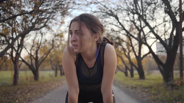 Portrait of Tired Sportive Girl Resting on Alley in the Autumn Park As Two Strong Sportsmen Running