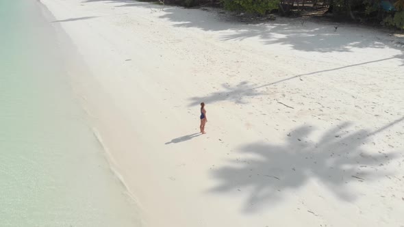 Aerial: Woman relaxing on white sand beach turquoise water tropical coastline