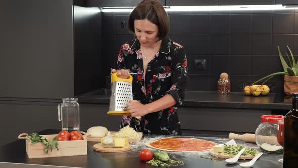 Female grates cheese, preparing traditional pizza in home modern kitchen