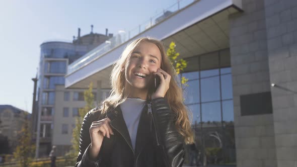 Beautiful Young Woman is Walking on the City Street While Talking with Her Friend on the Smartphone