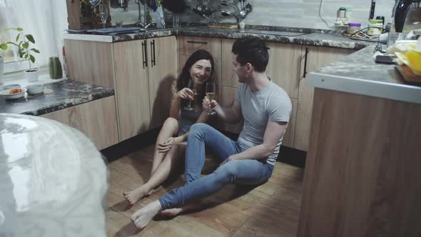 Affectionate Young Family Couple Sitting on the Floor of Cozy Kitchen and Celebrating Anniversary