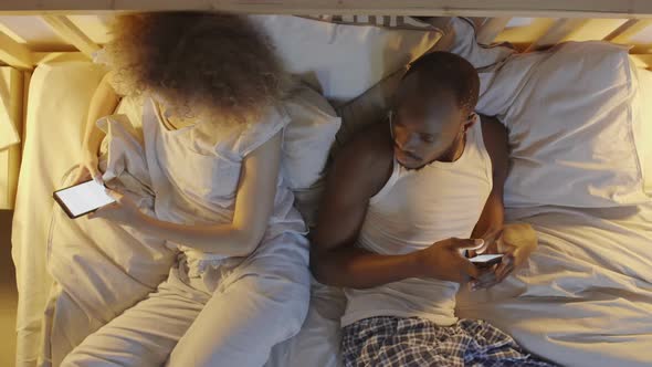 Multiethnic Couple with Phones in Bed